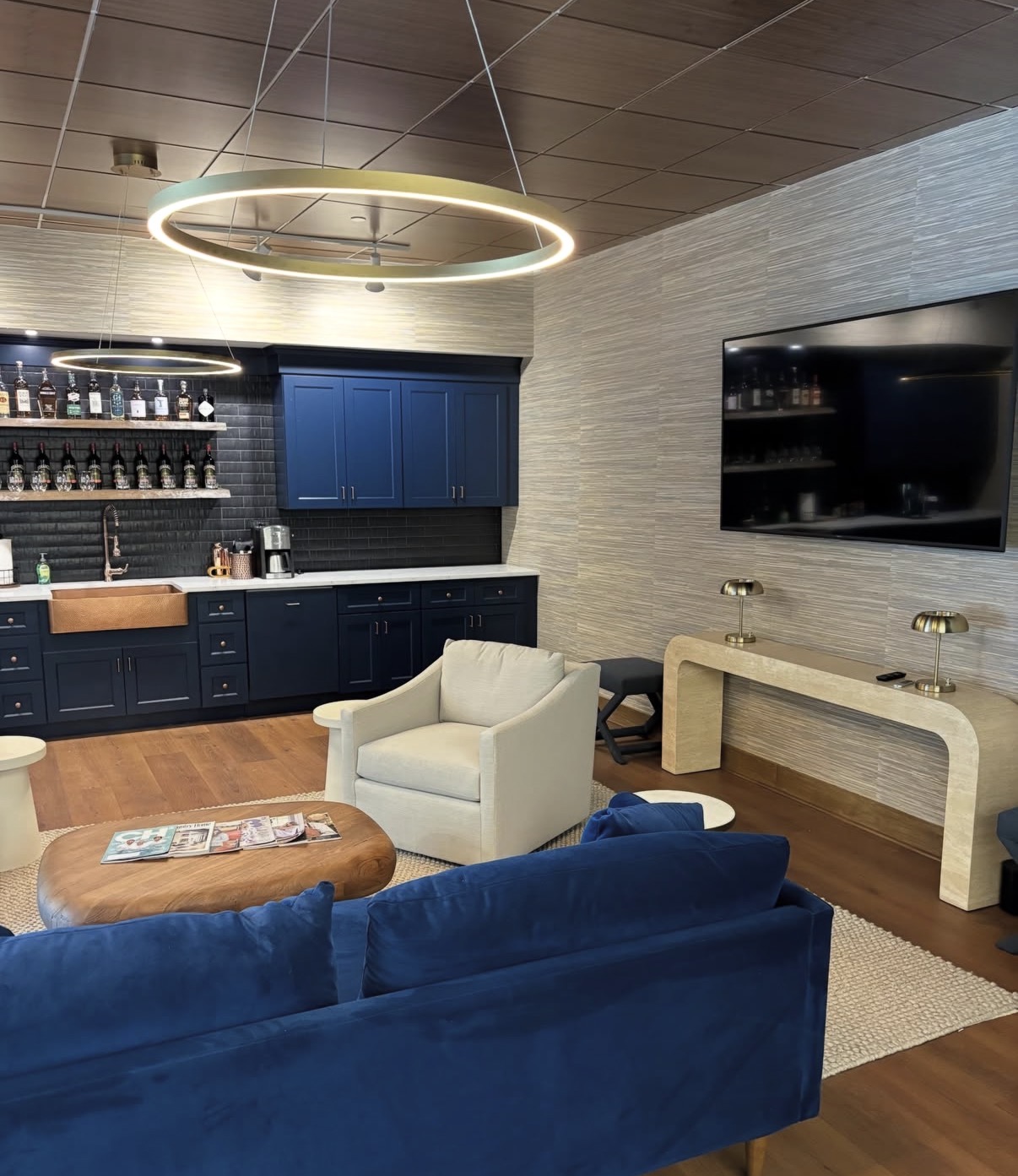 Textural grasscloth wrapping a bar and media lounge with navy cabinetry and ring pendants