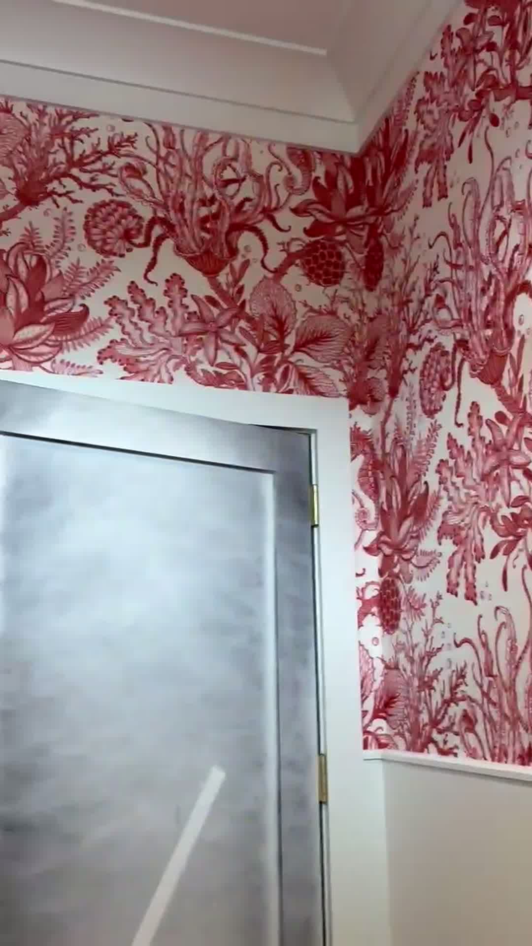 Coral-red seahorse and sealife wallpaper wrapping a powder room corner beside a mirrored door