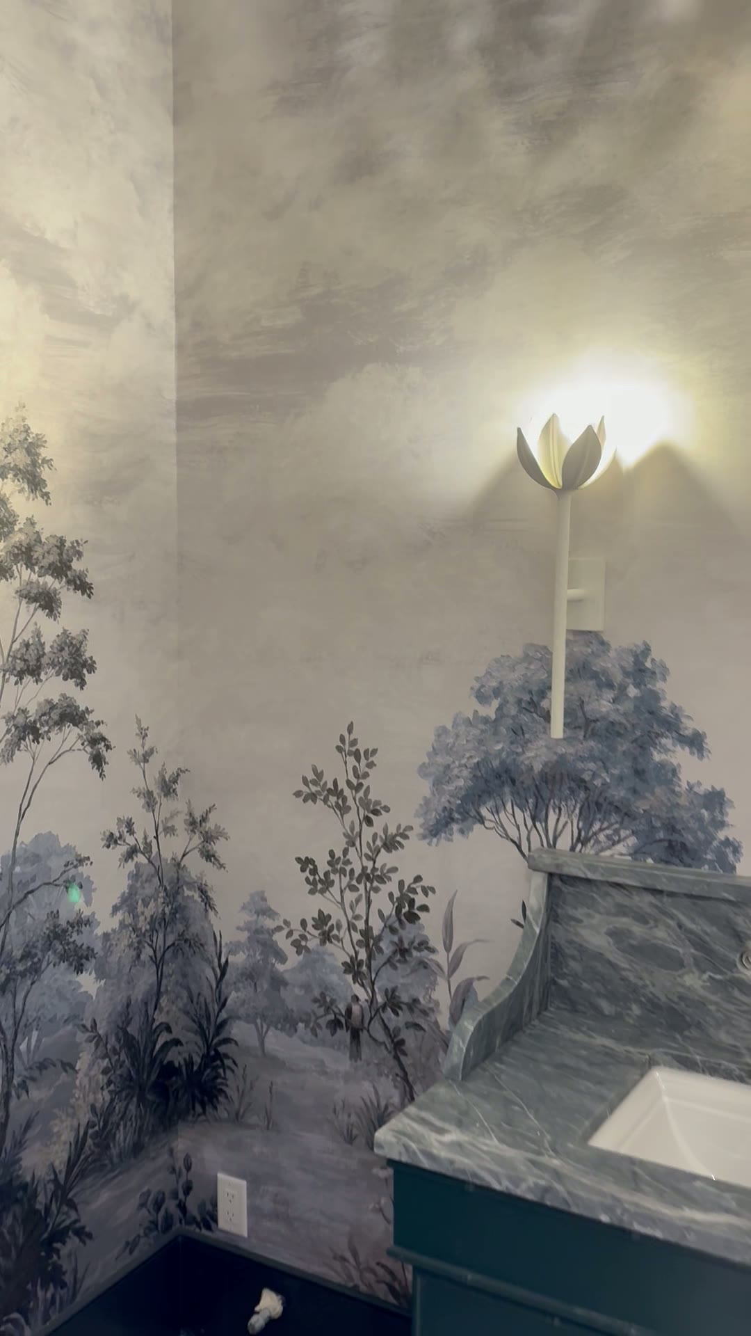 Moody blue-gray landscape mural powder room with green marble vanity and tulip sconce