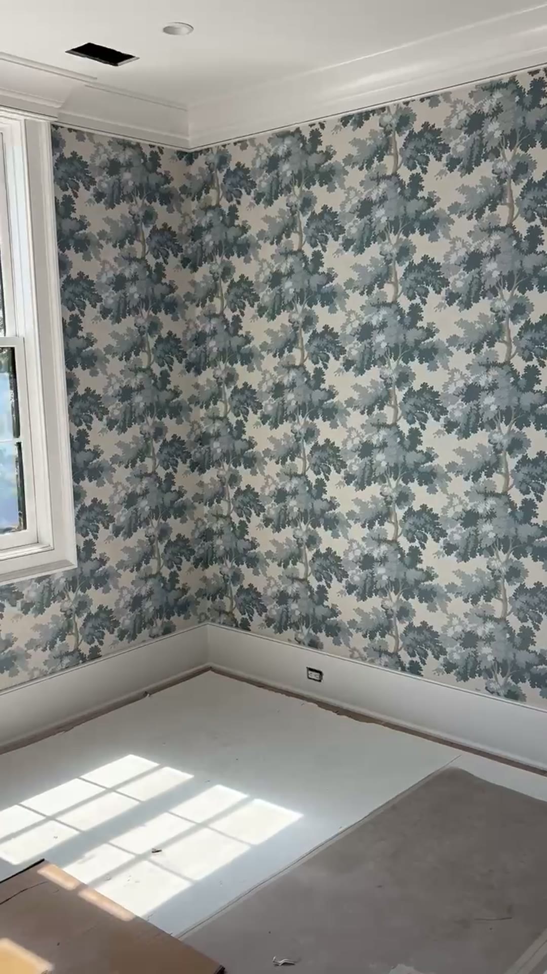 Blue oak-tree pattern wallpaper wrapping a corner bedroom with tall sash window